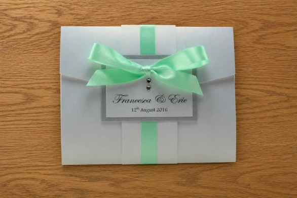 Bridal white pocketfold wedding invitation with hints of metallic silver and a tied mint ribbon bow